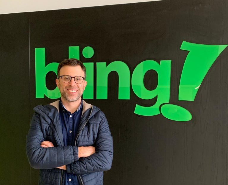 Marcelo Navarini está de braços cruzados em frente do logo da bling