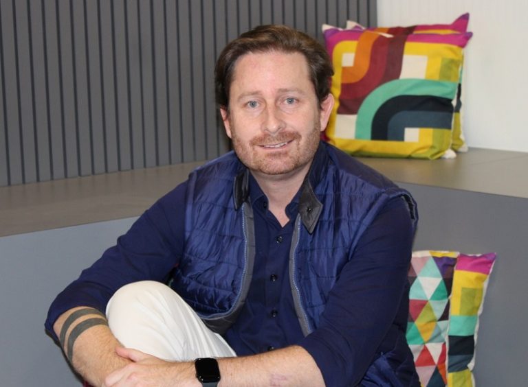 Luiz Iannini, da Neo, está sentado na frente de almofadas coloridas