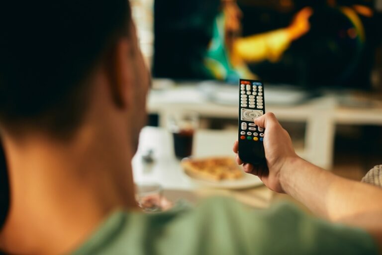 Homem na frente da TV mexendo no controle remoto